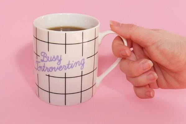 Person holding mug that says 'Busy Introverting'
