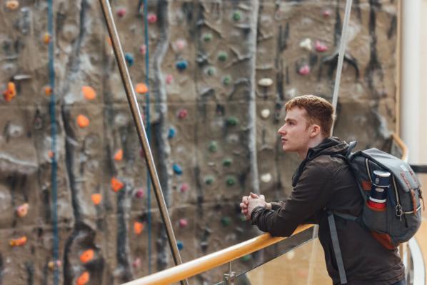 Male student stands in front of climbing wall in the PEC