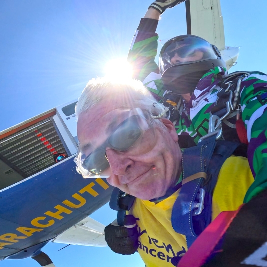 close-up looking towards the sky of a man strapped to an instructor and skydiving out of a plane